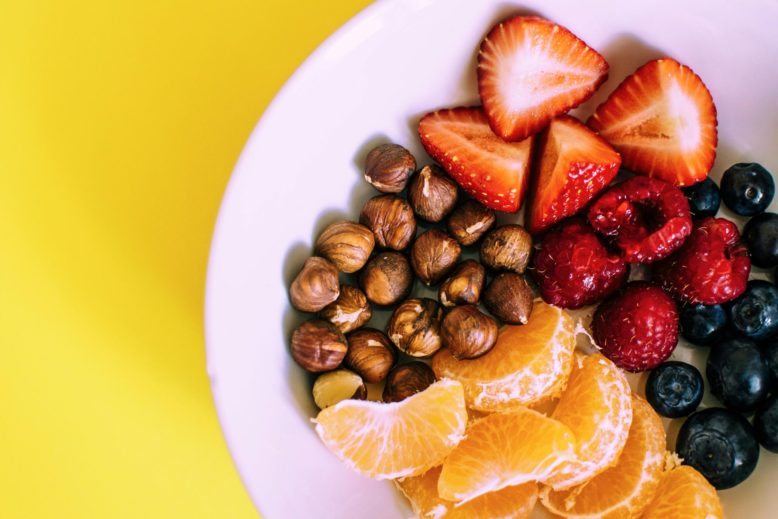 Eat Food That Looks Like a Crayon Box: The Simple Secret to Living Longer 🌈 Close-up of a bowl with fresh fruits and nuts against a vibrant yellow backdrop.