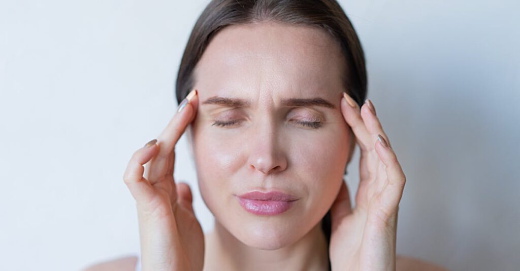Close-up of a woman with closed eyes holding her temples, showing signs of a migraine or headache.