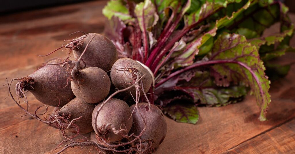 Bundle of fresh organic beetroots with vibrant green leaves on a wooden surface.
