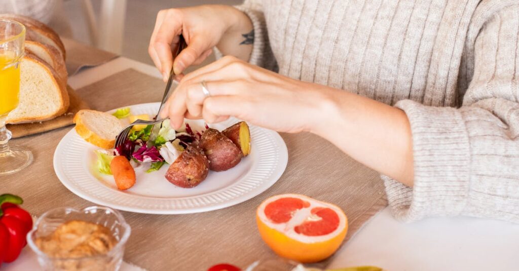 A woman in a cozy sweater enjoys a healthy breakfast with fruit and salad indoors.