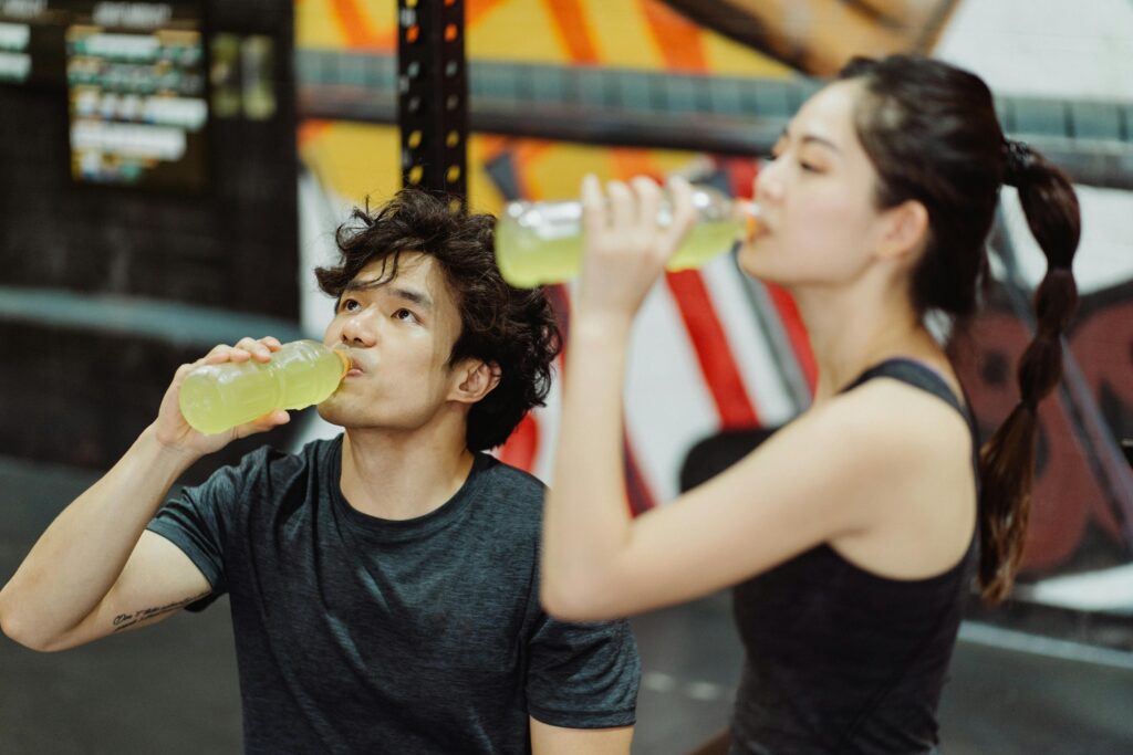 Fit Asian couple hydrating at the gym after an intense workout. Refreshing drink break.