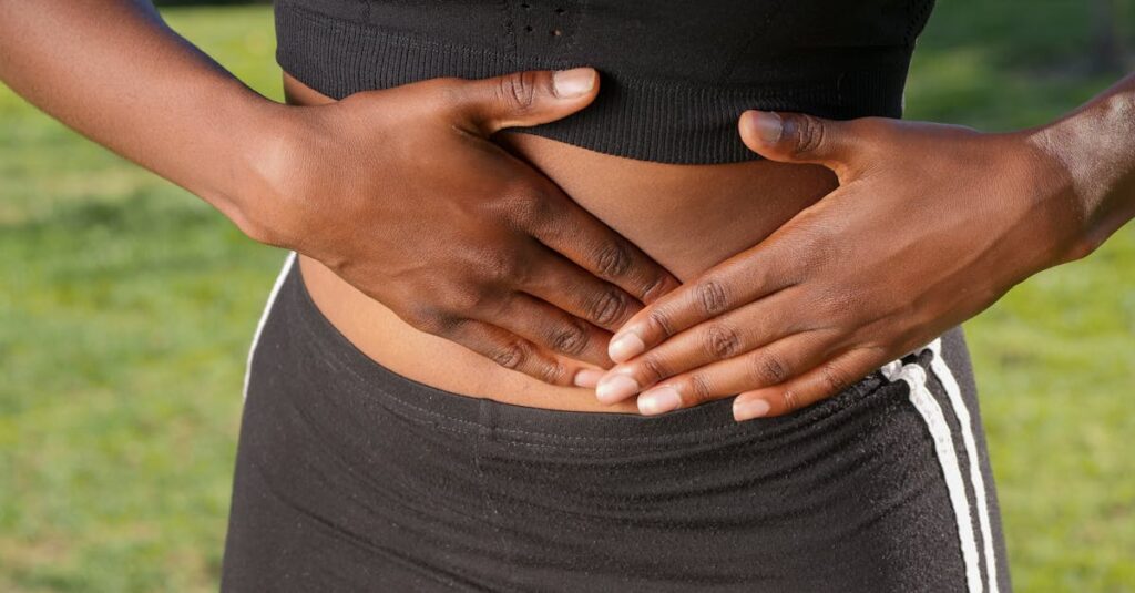 Close-up of a person holding their stomach, indicating abdominal pain outdoors.