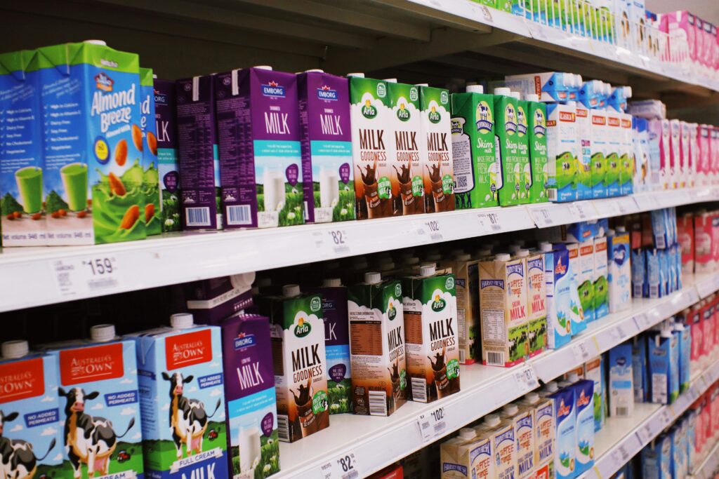 Various milk cartons displayed on shelves in a bright supermarket aisle.