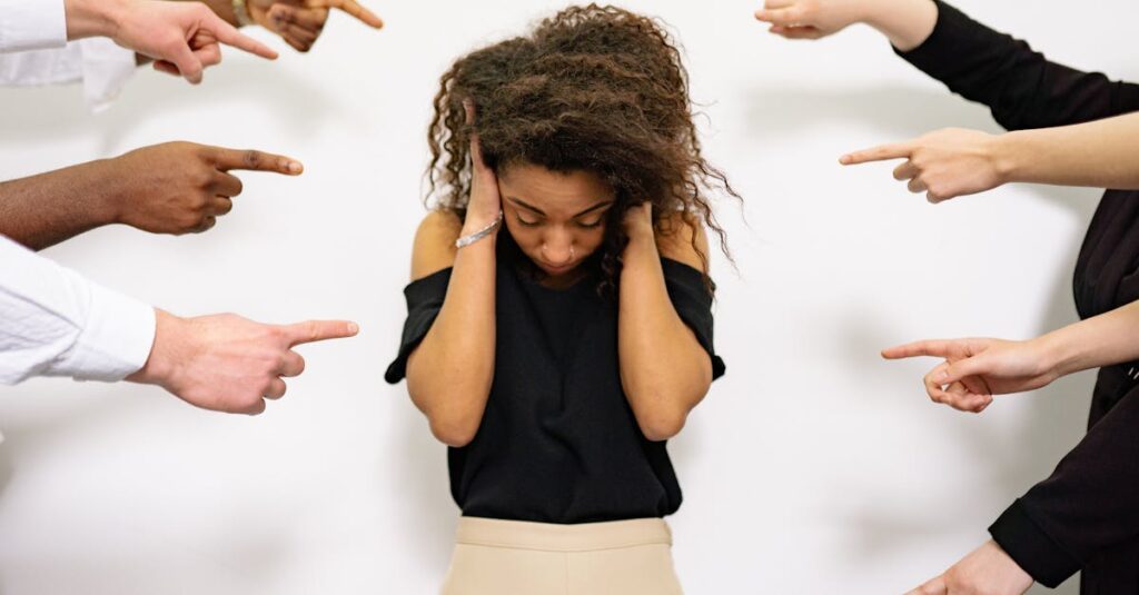 A young woman with curly hair looks distressed as multiple hands point accusatory fingers at her.