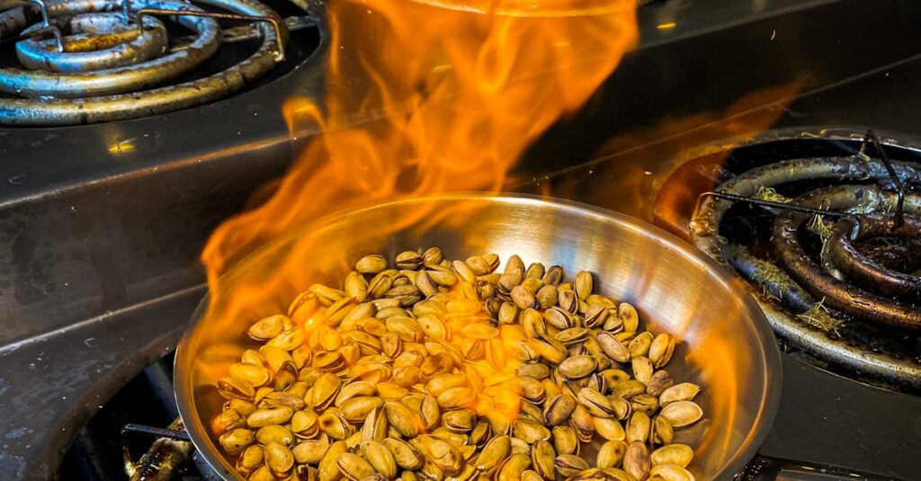 Pistachios roasting in a pan over a stove with visible flames, captured indoors.