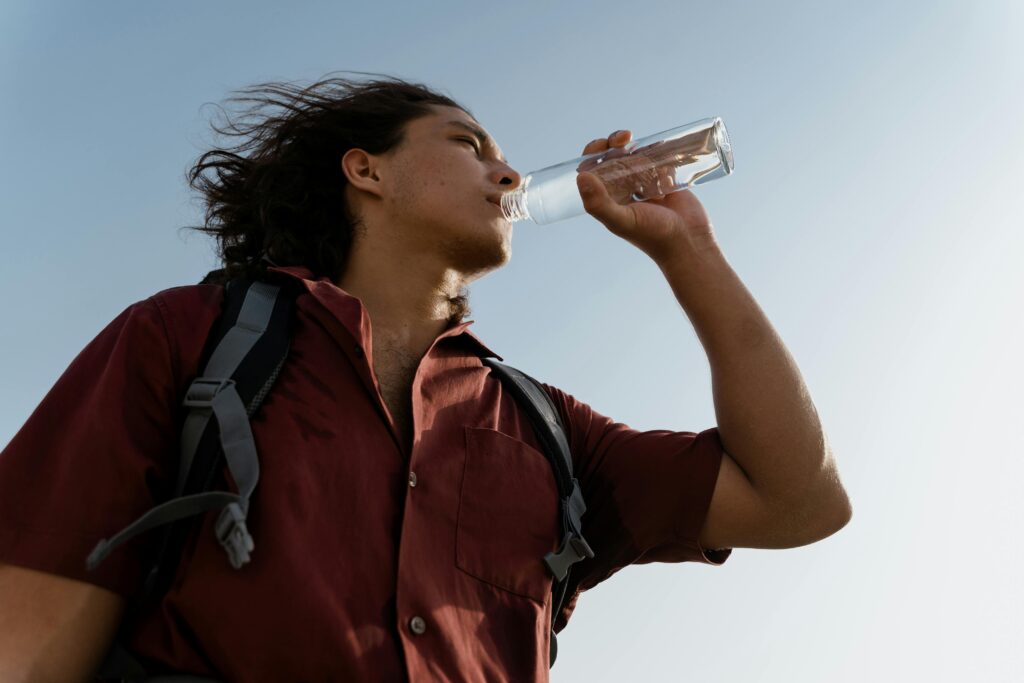 A man drinks water while hiking under a clear blue sky.