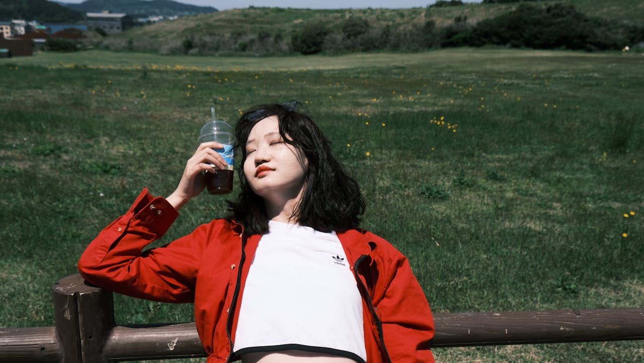 Home Young woman resting with a drink in a sunny field, enjoying the outdoors.