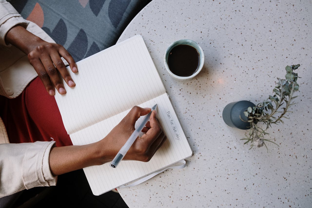 About Person writing in a planner with coffee at a café, focusing on planning and productivity.