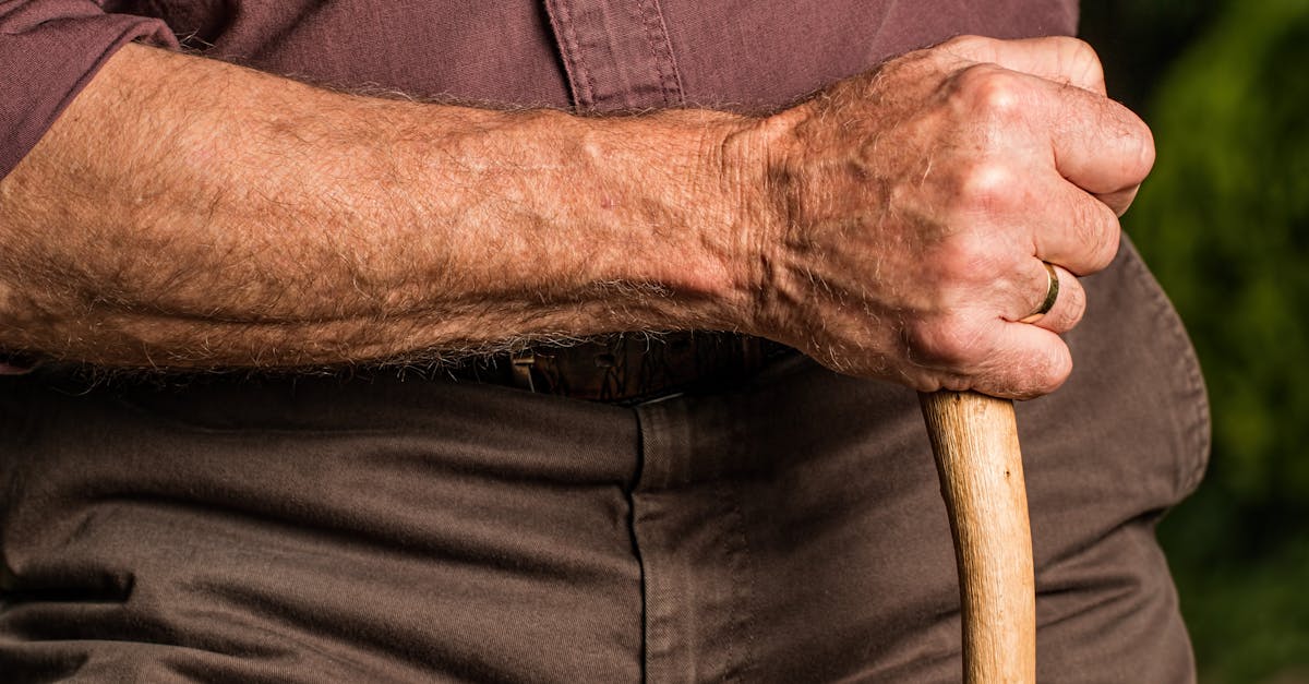 Close-up of a senior adult's hand gripping a wooden walking cane outdoors, symbolizing support and aging.