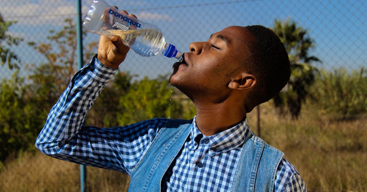 Side profile of a young man enjoying water from a bottle in a sunny outdoor setting.