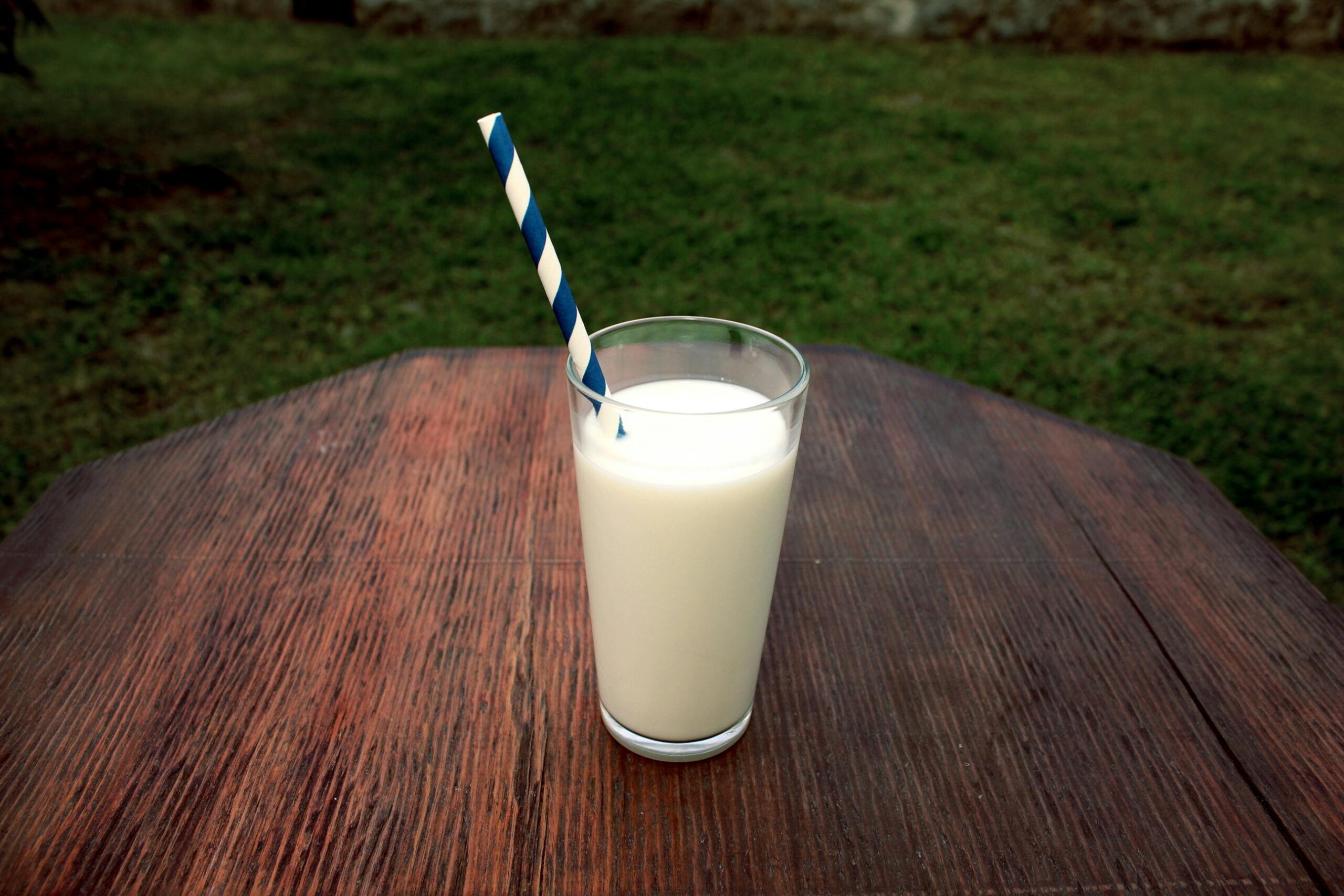 A refreshing glass of milk with a straw on a wooden table set outdoors, perfect for a healthy break.