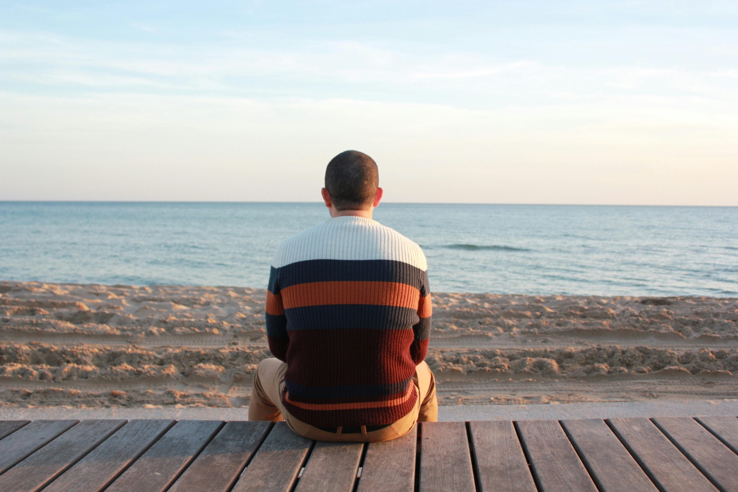 A man sitting on a wooden pier overlooking the tranquil ocean horizon.