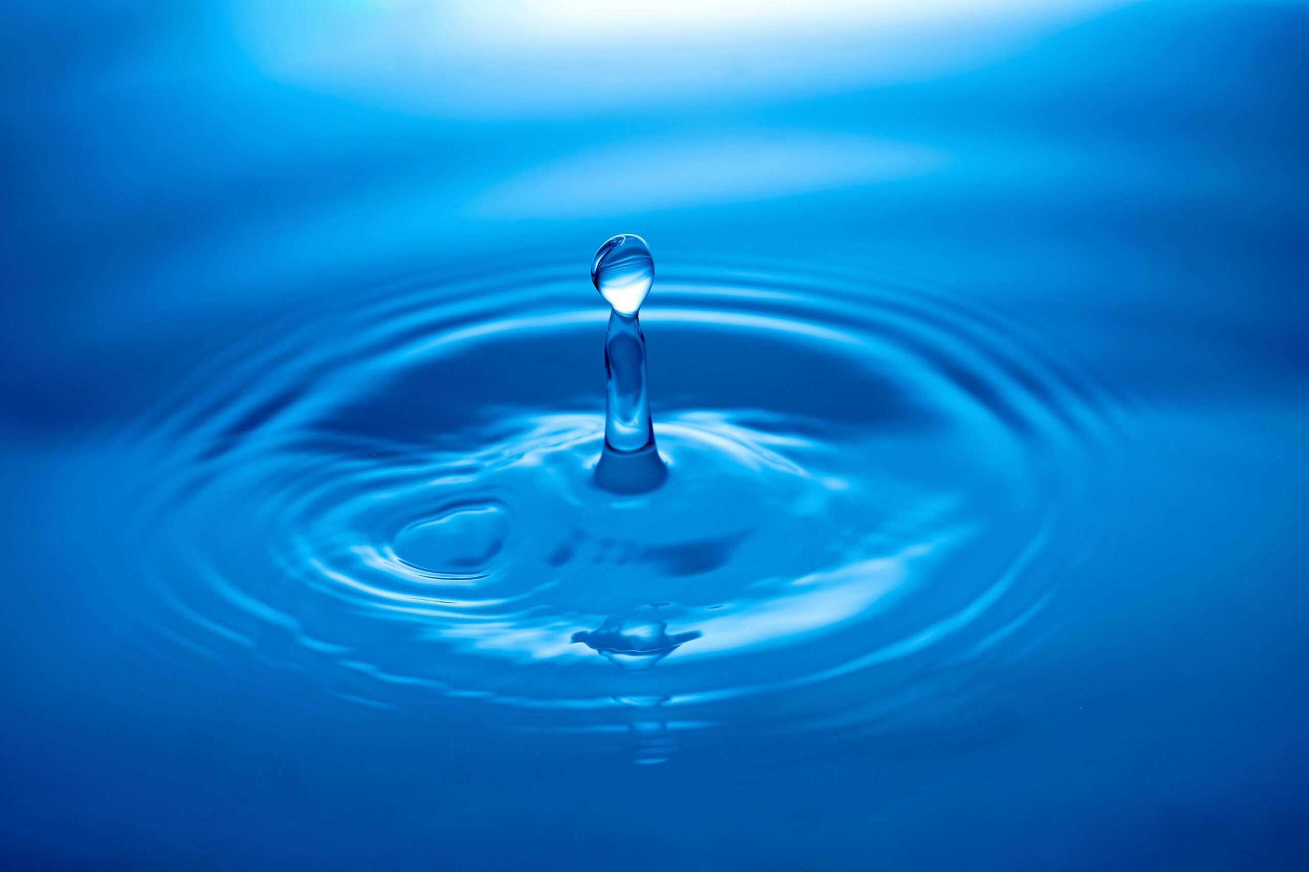 Capture of a water droplet creating ripples on a blue surface showcasing tranquility and clarity.