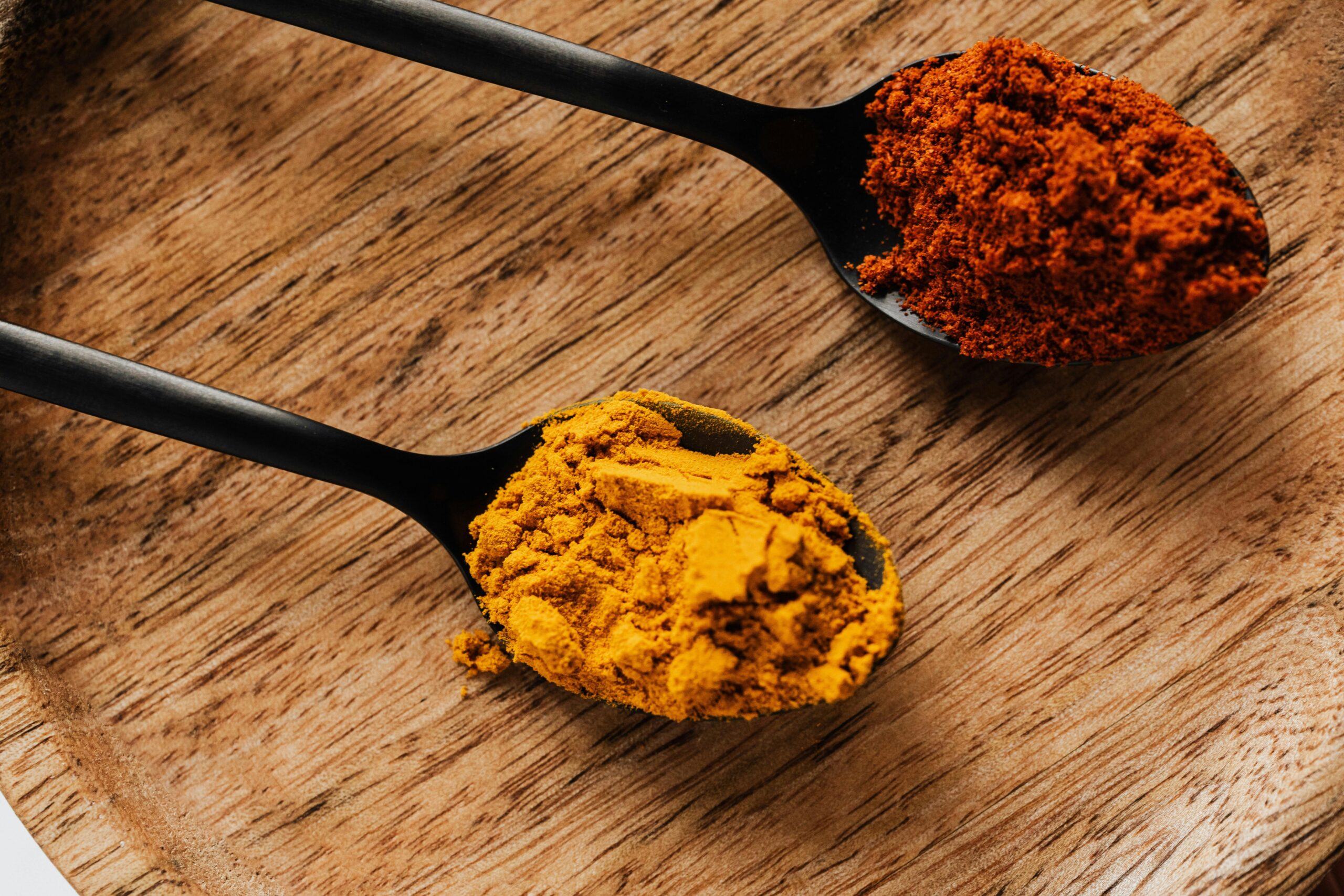 Close-up of turmeric and paprika spices on black spoons on a wooden tray.