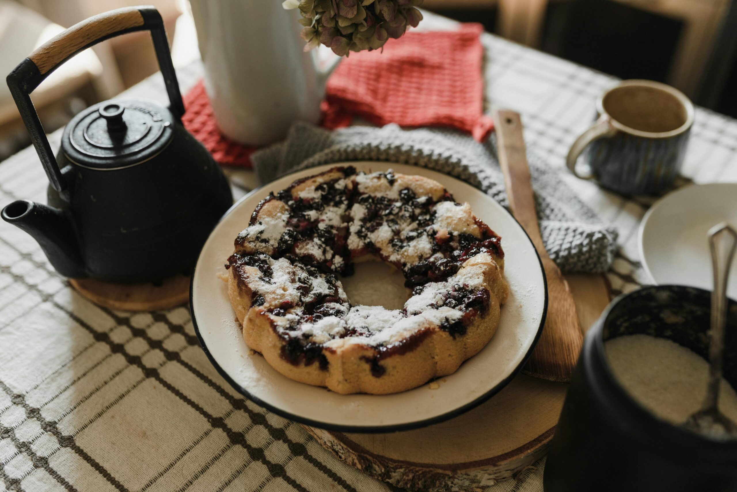 Cozy table setup featuring a homemade blueberry cake, tea, and rustic elements.