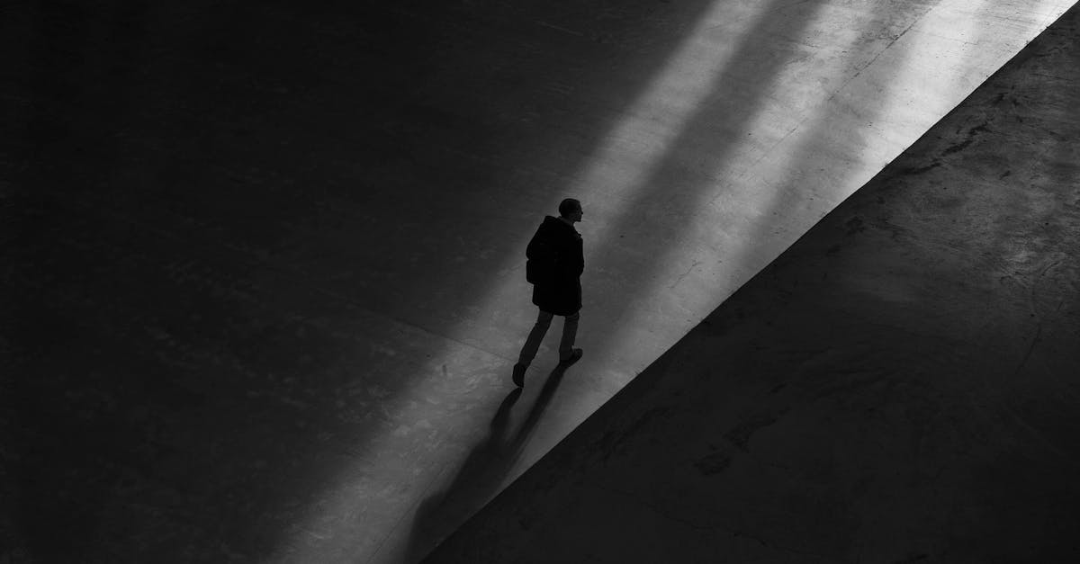 Black and white photo of a man walking through shadows on a deserted pavement, creating a moody silhouette.